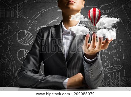 Closeup of business woman in suit presenting flying aerostate among clouds in her palm with business sketches on background. 3D rendering.