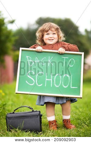Cute caucasian little girl holding chalkboard written back to school. With a smile. Ready and happy back to school. Fall outdoors autumn day education concept back to school concept. Early developement early education.