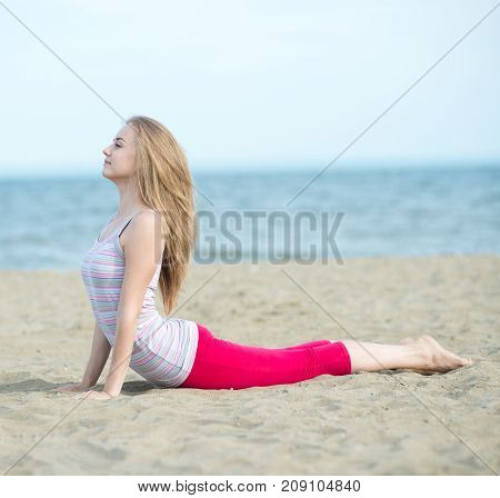 Young lady practicing yoga. Beautiful woman posing at the summer sand beach. Workout near ocean sea coast. Beautiful fit tan girl. Fitness model caucasian ethnicity outdoors. Weight loss exercise. Meditation.