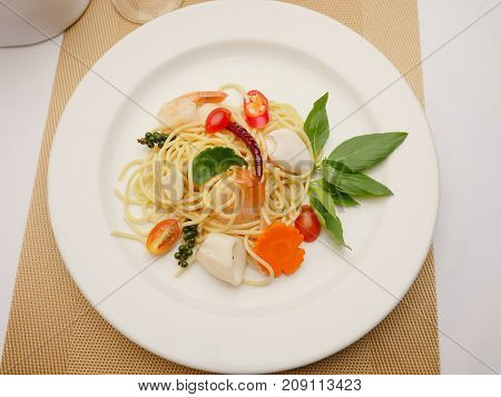 Spaghetti stir fried. It has a spicy taste with shrimp and squid in white plate.