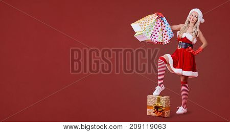 Girl in Santa Claus costume with gift packages on red background. Place for text.