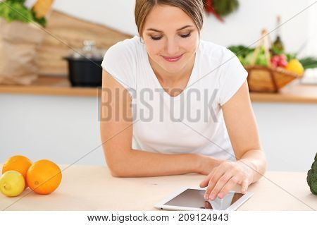 Young woman is making online shopping by tablet computer and credit card. Housewife found new recipe for cooking in a kitchen.