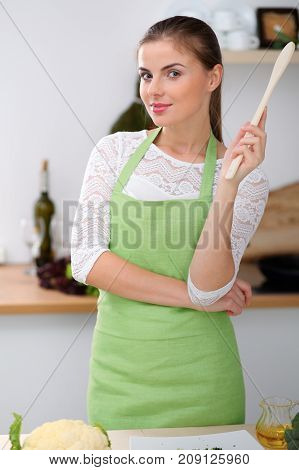 Young woman in the green apron is  cooking in the kitchen. Housewife thinking about the menu while holding a wooden spoon in his hand