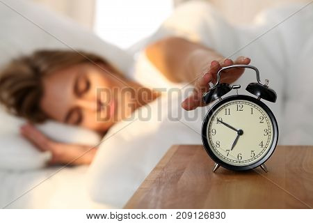 Sleepy young woman stretching hand to ringing alarm willing turn it off. Early wake up, not getting enough sleep, getting work concept