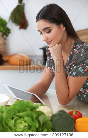 Young hispanic  woman is making online shopping by tablet computer and credit card. Housewife found new recipe for  cooking in a kitchen