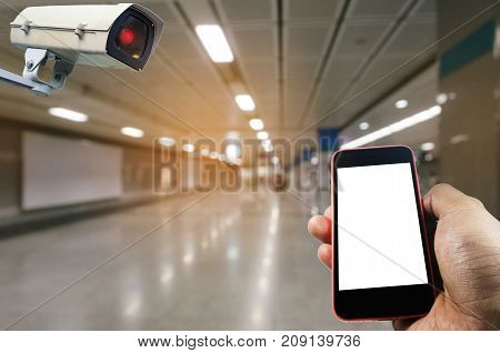 hand using mobile phone with blank screen and security camera system operating with blurred image of subway train station or airport internet surveillance security and safety technology concept