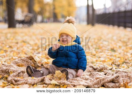 happy little boy in the sun in autumn, sitting in leaves and yellow cute hat