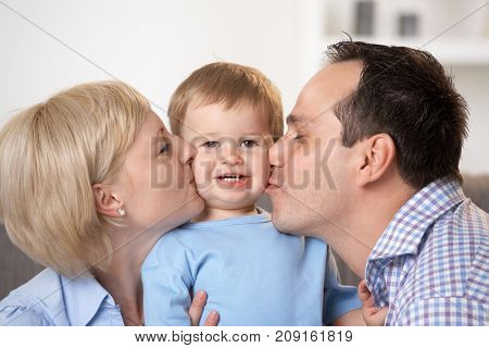 Portrait of happy family, father and mother kissing baby boy.