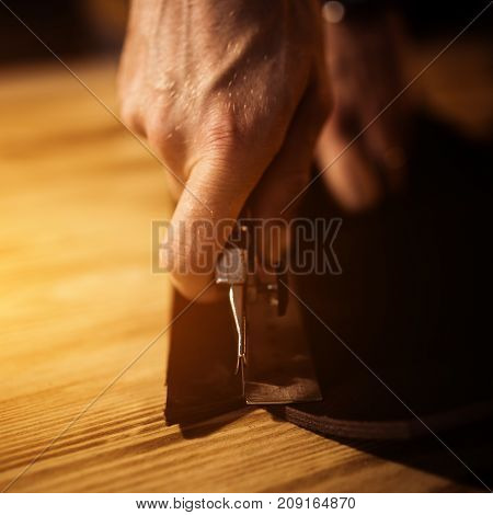 Working process of the leather belt in the leather workshop. Man holding crafting tool and working. Tanner in old tannery. Wooden table background. Close up man arm. Warm Light for text and design.