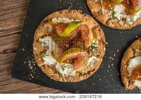 Canape or crostini with multigrain crispread with cream cheese and fig jam on a slate board. Delicious appetizer ideal as an aperitif.