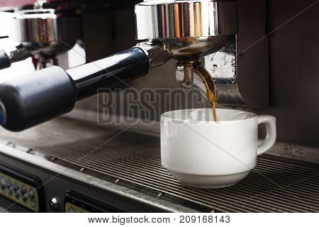 Coffee machine preparing hot bracing beverage. Espresso pouring into white porcelain cup. Small business and professional coffee brewing concept