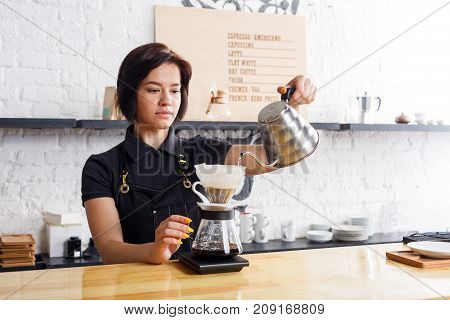Barista preparing pourover coffee at cafe counter. Portrait of young girl in uniform at her working place. Small business, occupation people and service concept, copy space