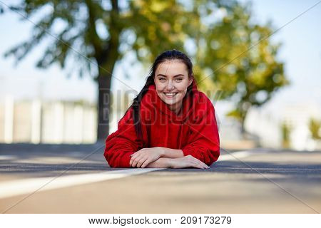 Beautiful girl in a red uniform the girl is lying on her stomach from on the street