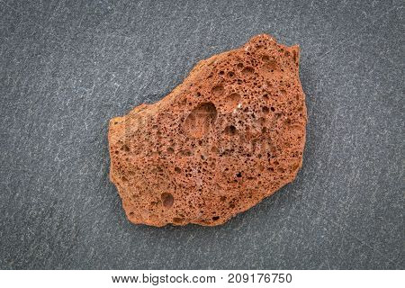 scoria igneous rock sample against gray slate stone, extrusive rock formed from fast-cooling lava blasted out of volcano