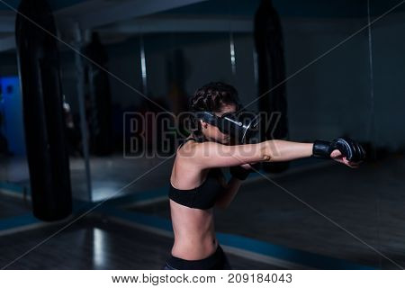 Young fighter boxer fit girl in VR glasses wearing boxing gloves in training in additional reality. Boxing game in virtual reality 360 degrees. Futuristic gaming
