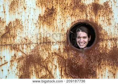 Abandoned and Stalkers. Young cute woman looks from the window of a rusty industrial objects. 