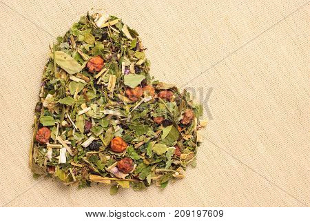 Dried herb leaves heart shaped on burlap jute surface. Herbaceous dry aromatic plant. Healing herbs herbal medicine concept.