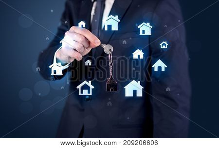 Businessman in suit holding keys with house graphics around and dark background