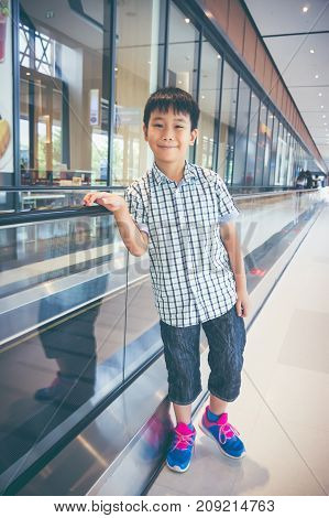 Happy Asian Child Standing And Smiling Near Electric Speedwalk In Modern Airport.