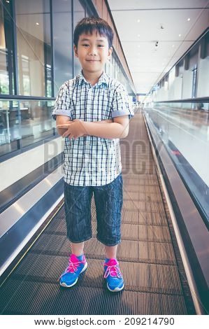 Happy Asian Child Standing And Smiling On Electric Speedwalk At Modern Airport.