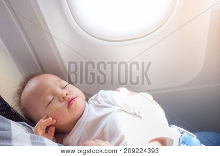 Cute little Asian 18 months / 1 year old toddler baby boy child sleeping on Airplane with copy spaceToddler boy sleeping on mother's laps while traveling in airplane Flying with children concept