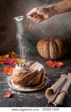Bundt cake with saffron and rum covered with white glaze on rustic background with autumn decorations