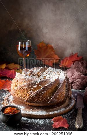 Bundt cake with saffron and rum covered with white glaze on rustic background with autumn decorations