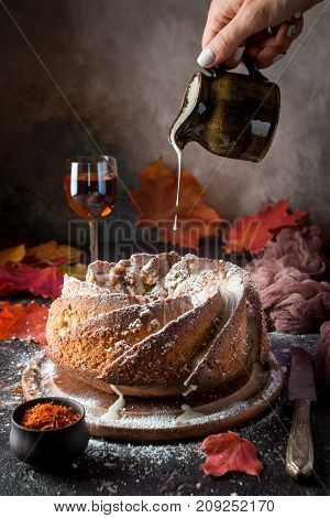Bundt cake with saffron and rum covered with white glaze on rustic background with autumn decorations