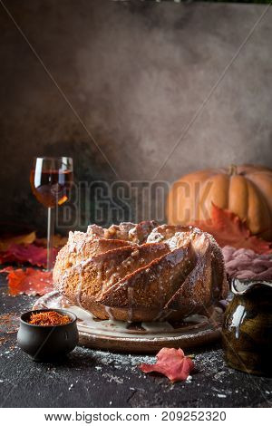 Bundt cake with saffron and rum covered with white glaze on rustic background with autumn decorations