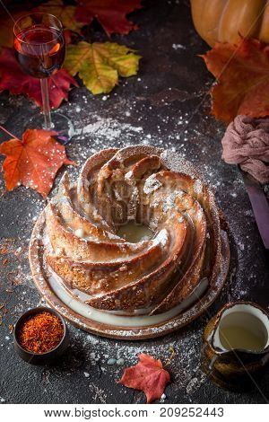 Bundt cake with saffron and rum covered with white glaze on rustic background with autumn decorations