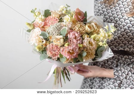 Mix flowers. Luxury bouquets in the girl's hands. on a light gray wall