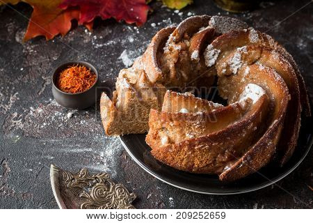 Bundt cake with saffron and rum covered with white glaze on rustic background with autumn decorations