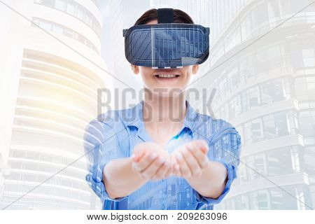 Take it. Happy young woman wearing a VR headset and handing a ball of light in her cupped hands while smiling broadly