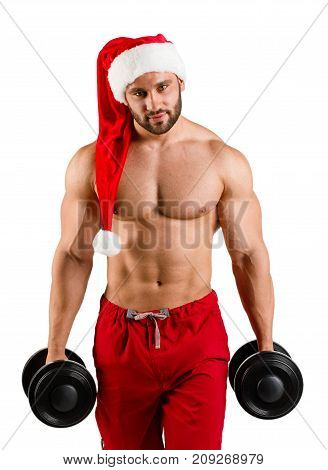 One sexual strong man with dumbbells in hand, young and sexy Santaclaus with muscular body in traditional red and white hat on studio. White background, isolated, vertical image