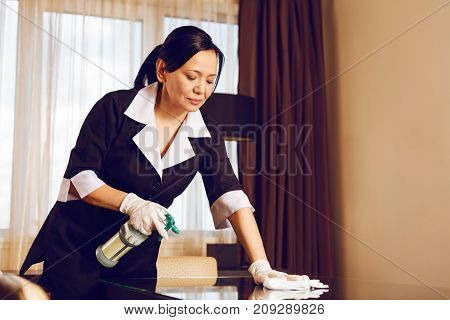 Let me clean it. Competent maid bowing head while looking downwards and preparing room for new guest