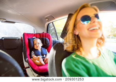 Young mother with her little son in the car. A woman driving and baby boy sitting in a car seat.