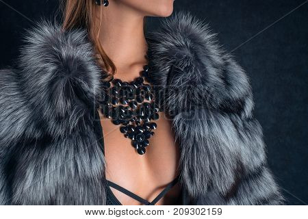 Luxurious young lady in an expensive necklace and earrings made of natural stones on a dark background