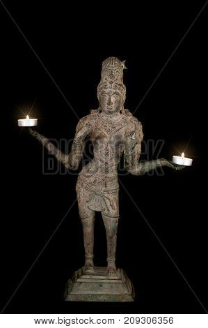 Hinduism and spiritual enlightenment with bronze statue of goddess Lakshmi holding burning candles with starburst lens flare. Religious iconography isolated against black background