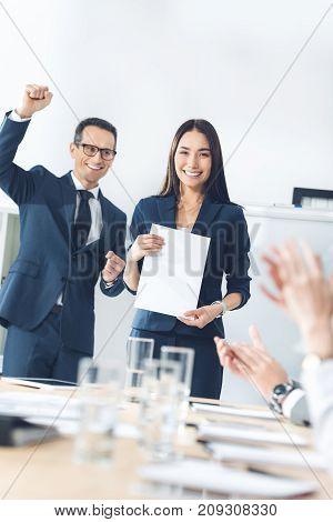 rewarded young manageress holding blank paper while colleagues clapping to her