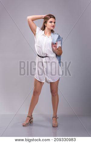 Portrait of a plus size female model posing in white dress over grey background. Beautiful woman with curvy figure.