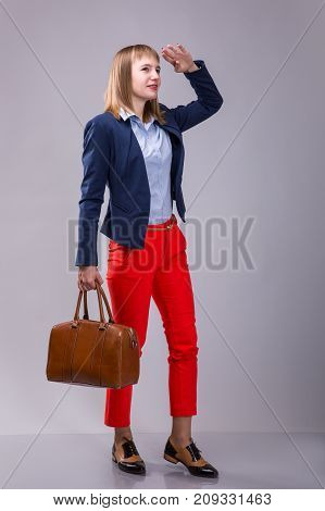 girl in red pants with a leather bag looking into the distance over gray background
