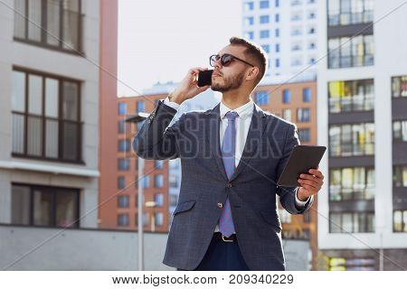 Real estate agent on background of modern city. Businessman is talking by mobile phone