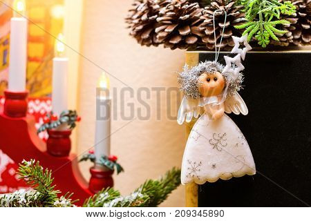 Christmas angel rag doll hanging on Christmas wreath with fir cones. Amid a festive candle holder with candles. Celebration of New year and Christmas at home