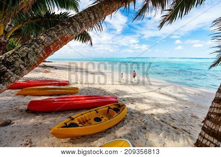 Kayaks at beautiful tropical beach with palm trees, white sand, turquoise ocean water and blue sky at Cook Islands, South Pacific