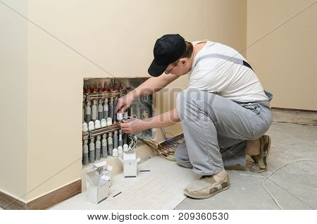 Installation of home heating. Men attaches the servo valve drive underfloor heating.