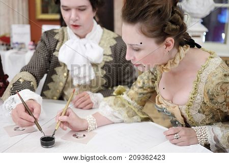 MOSCOW - SEP 16, 2017: Man and woman write by feathers and ink at Great Catherine Ball (dance party) in Tsaritsyno