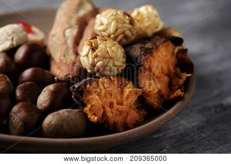 closeup of an earthenware bowl with some chestnuts, some panellets and a roasted sweet potato, as a typical snack eaten in All Saints Day in Catalonia, Spain, called castanada, on a wooden table