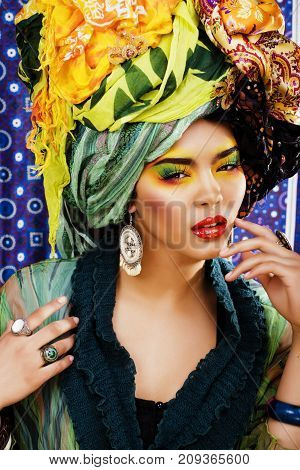 beauty bright woman with creative bright make up, many shawls on head like cubian, ethno look closeup