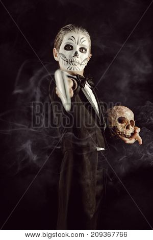 Portrait of a child boy with carnival make-up of a skeleton wearing elegant tail-coat. Studio shot over black background. Halloween. Dia de los muertos. The Day of the Dead.