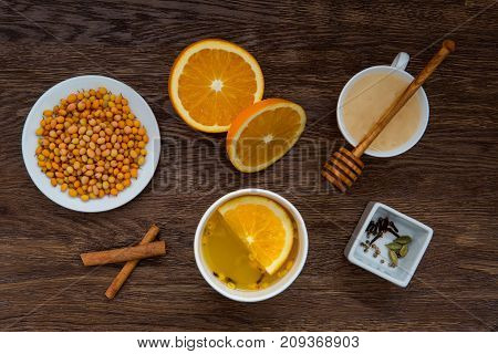 Winter warming tea and ingredients. Cup of tea, orange, sea buckthorn, honey and cinnamon on wooden table. anti-cold products. Top view
